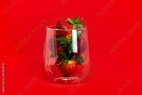 Strawberries in a glass transparent beaker with highlights close-up on a red background. Romantic background.