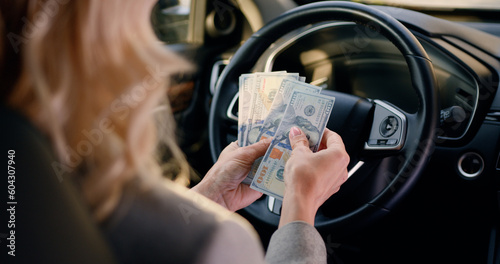 Close-up female hands behind steering wheel in luxury car counting cash financial profits in the parked car.