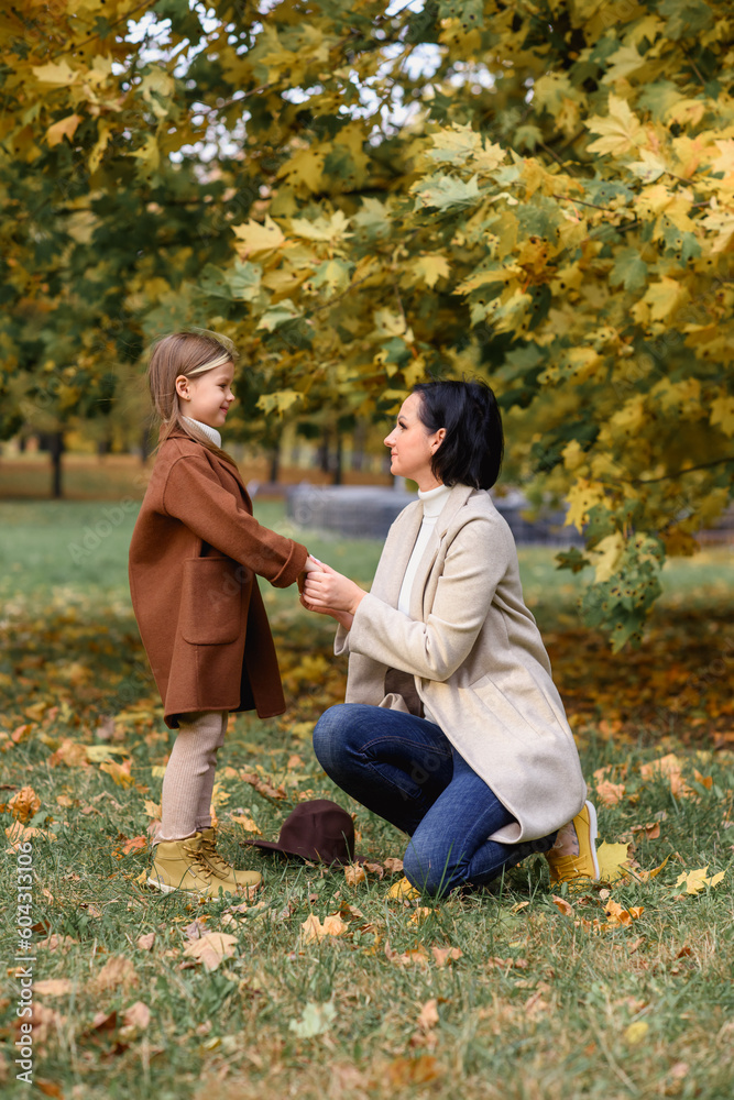 little beautiful girl with her mother hugging and kissing in the park in autumn in golden leaves little beautiful girl with her mother hugging and kissing in the park in autumn in golden leaves