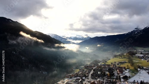 Saint Jean de Sixte and its surroundings. Zoom in timelapse of the running clouds in snowy mountains with city and lighty sun on the foreground, Alpes France. photo