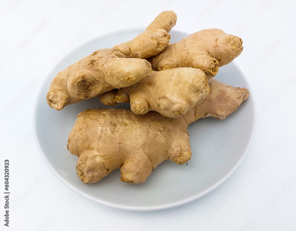 Fresh ginger rhizome on a white plate, isolated on white background with copy space. Close-up view. Fresh ginger rhizome on a white plate, isolated on white background with copy space. Close-up view.