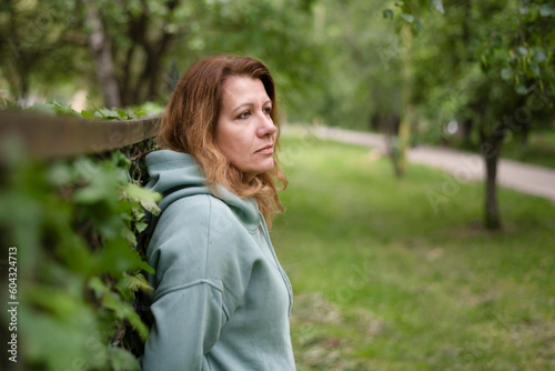 Middle-aged woman looks forward and to the side, upset, tired after work, resting in nature in park after a stressful day, woman needs rest and help at work