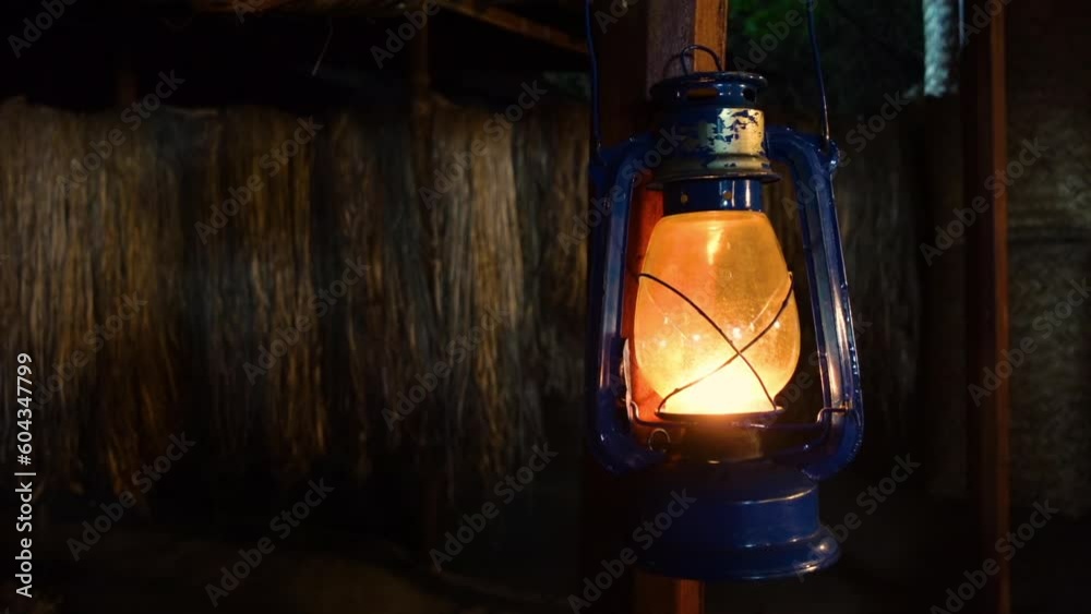 A kerosene lantern hangs from the balcony of a bamboo village house. 