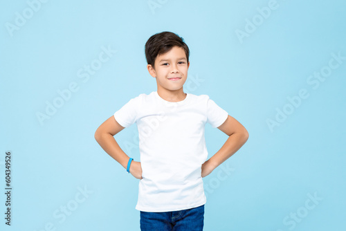 Cute mixed race boy smiling with arms akimbo in studio isolated light blue color background photo