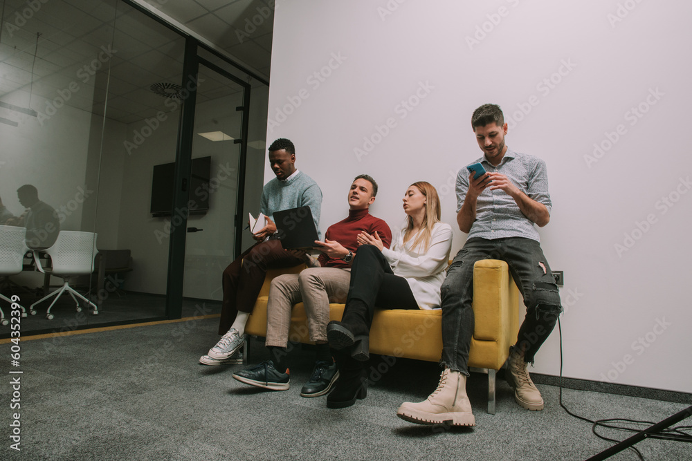 Multiracial colleagues spending their free time at work the way they want it, sitting on a sofa, checking phones, playing music on lap top, singing Multiracial colleagues spending their free time at work the way they want it, sitting on a sofa, checking phones, playing music on lap top, singing