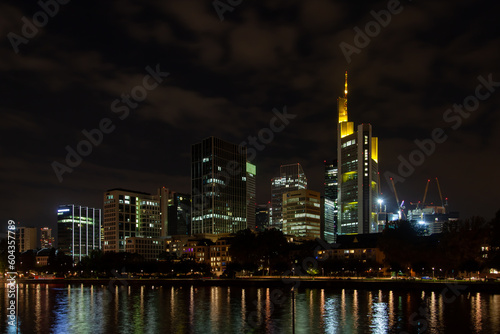 Nighttime of Frankfurt cityscape highlighting the river, lit skyscrapers, and their reflection. Perfect for urban backgrounds and ads.