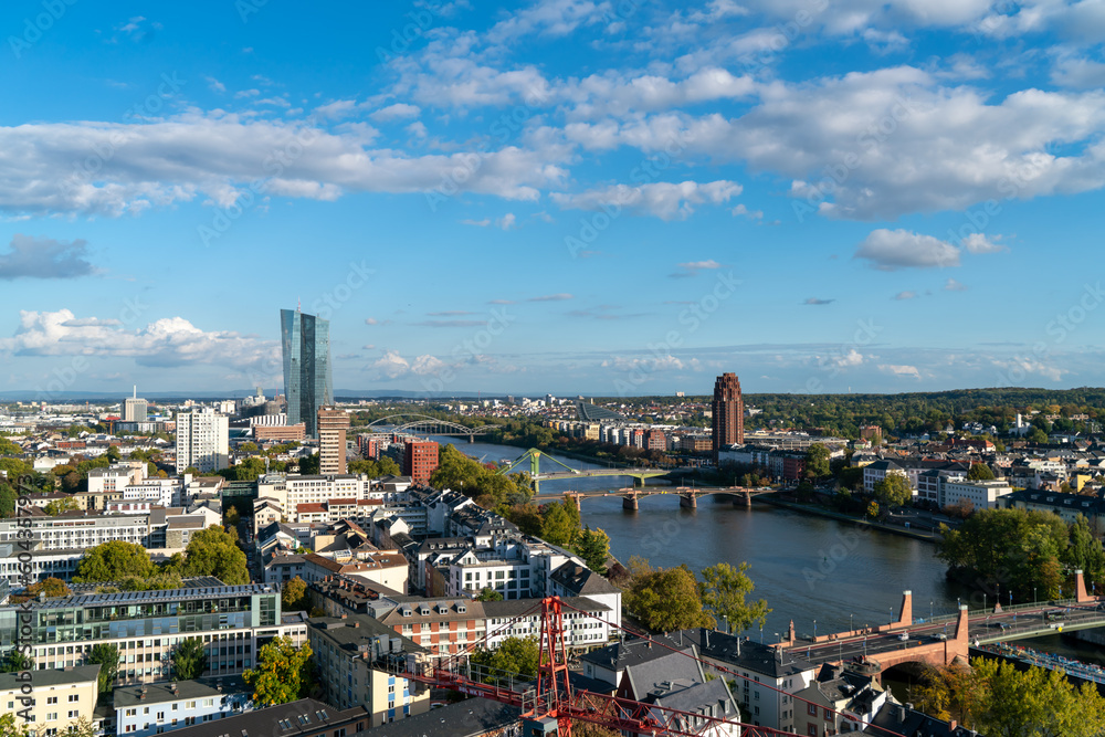 Daytime  of Frankfurt skyline featuring skyscrapers, bridge and river with partly cloudy skies during autumn season in Germany.