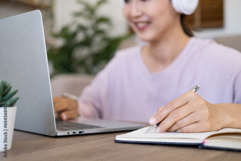 Close up hand - Attractive female student learning language, watching online webinar, listening audio course, Focused woman wearing headphones using laptop writing notes, e-learning education concept Close up hand - Attractive female student learning language, watching online webinar, listening audio course, Focused woman wearing headphones using laptop writing notes, e-learning education concept