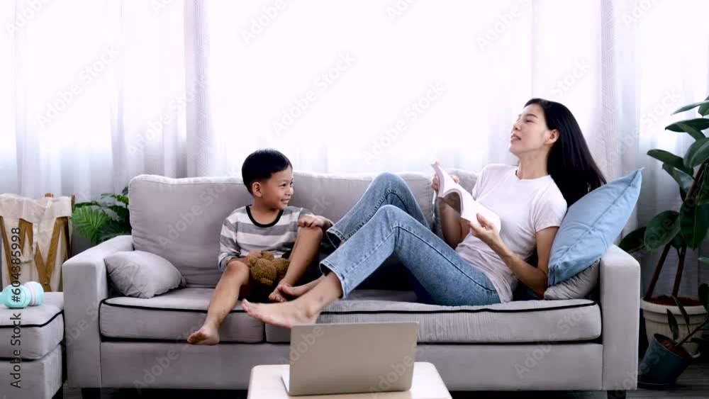 Asian beautiful mother and son read favorite book together on weekends, young woman and adorable boy lying down on sofa reading a comic book in the living room with happiness and fun. Asian beautiful mother and son read favorite book together on weekends, young woman and adorable boy lying down on sofa reading a comic book in the living room with happiness and fun.