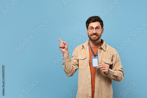 Smiling man showing VIP pass badge on light blue background, space for text