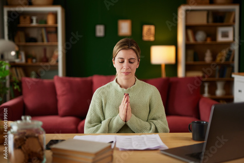 Calm young woman meditating to reduce stress working on computer at home office