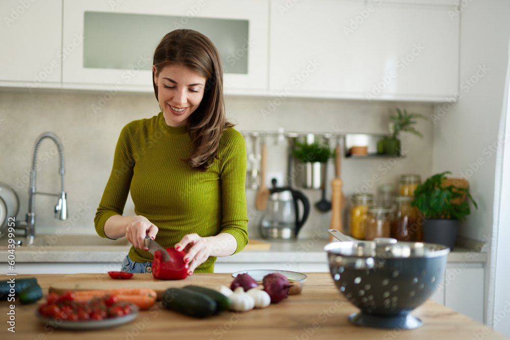 Woman chopping red bell pepper on the wooden board in the kitchen