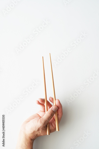 Right hand holding wooden chopsticks, ready for using, isolated on white, vertical frame, bottom to top, view from above