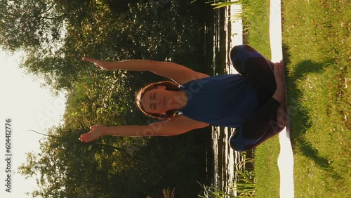 Peaceful relaxing woman practicing yoga on mat in park near lake. Vertical video photo