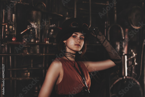 Classy teen girl model in steampunk image in retro brown dress and top hat looking at camera. Toned image of teenage girl actress 15-16 year old in industrial room. Adventure concept. Copy ad space