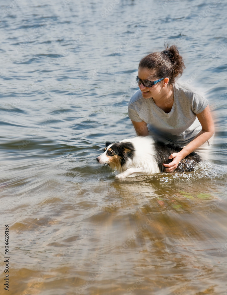 young mature woman playing with her sheepdog in the water - motion picture