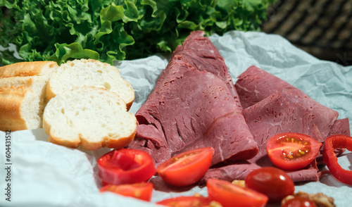 Deli meat cold cut on paper with vegetables, cherrry tomatoes, red paprica pepper, walnuts and lettuce salad leaves, french baguette photo