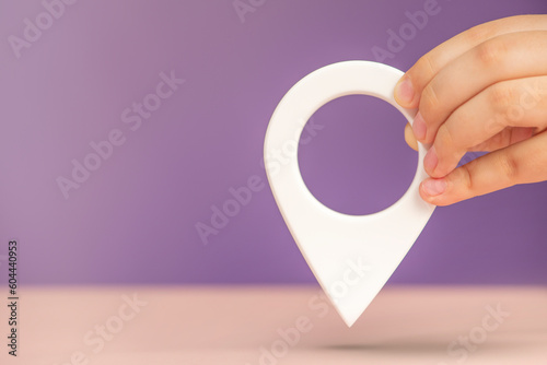 Pin icon or travel nautical map. GPS direction indicator. A hand holds a location sign on a purple background. Laying a route, finding a location. copy space.