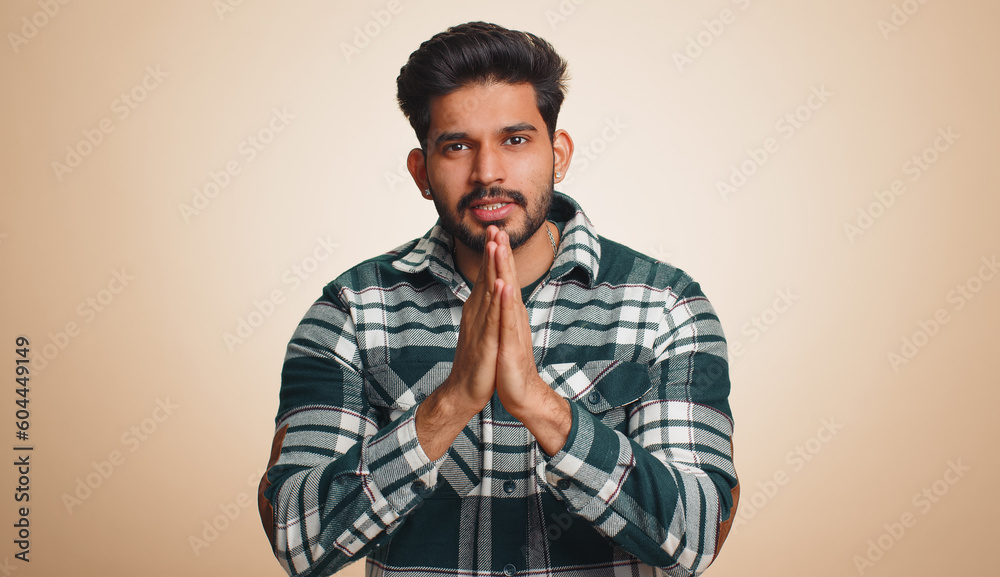 Please, God help, forgive me. Indian man praying, looking upward and making wish, asking with hopeful imploring expression, begging apology. Handsome hindu guy isolated on beige studio background