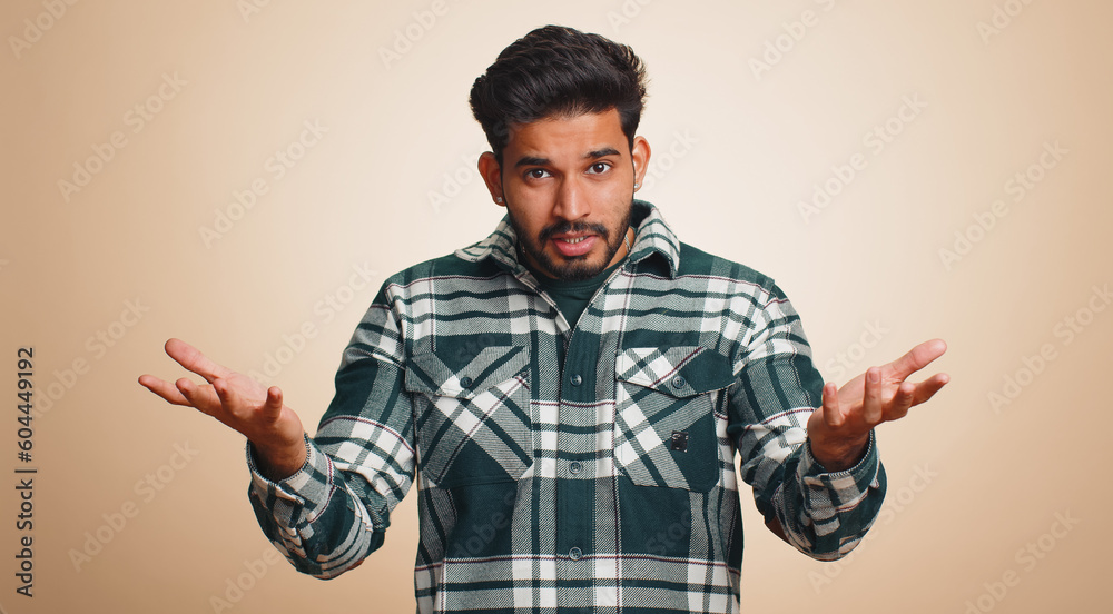 What Why. Sincere irritated indian man raising hands in indignant expression asking reason of failure demonstrating disbelief irritation by trouble. Handsome confused hindu guy on beige background - obrazy, fototapety, plakaty 