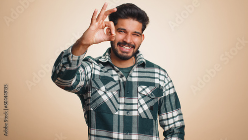 Ok. Joyful happy indian man in shirt looking approvingly at camera showing approve feedback gesture like sign positive something good. Handsome guy alone on beige background. People sincere emotion