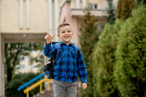 Cheerful mischievous Caucasian schoolboy in blue shirt and school jacket posing showing approval gesture, class. Back to school.