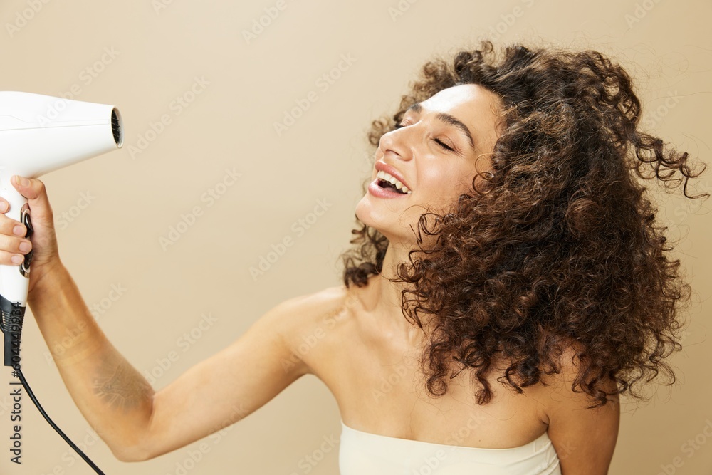 Woman dries curly afro hair with blow dryer, home beauty care styling  products hair, smile on beige background Stock Photo | Adobe Stock