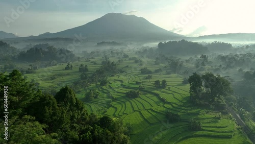 2023 - Excellent aerial view swooping over rice terraces towards a misty mountain in Sideman, Bali, Indonesia.