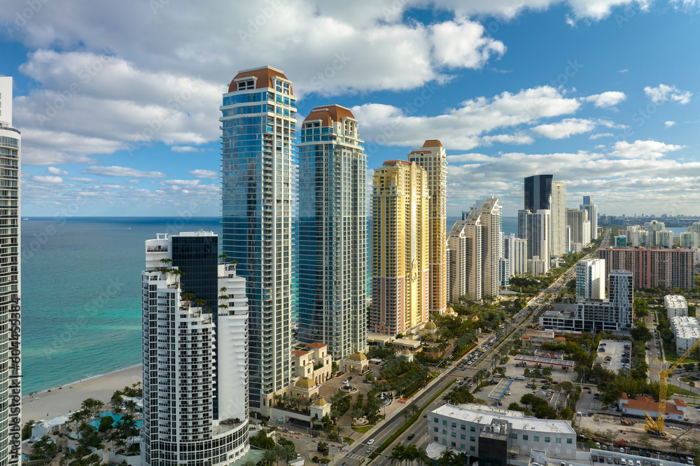 Obraz premium View from above of luxurious highrise hotels and condos on Atlantic ocean shore in Sunny Isles Beach city. Urban street with busy traffic. American tourism infrastructure in southern Florida