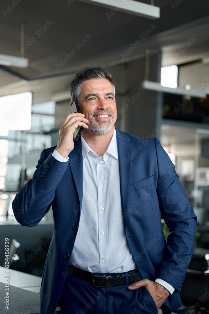 Happy confident middle aged business man talking on mobile phone in office. Successful professional businessman executive entrepreneur wearing suit holding telephone making corporate call on cell. Happy confident middle aged business man talking on mobile phone in office. Successful professional businessman executive entrepreneur wearing suit holding telephone making corporate call on cell.