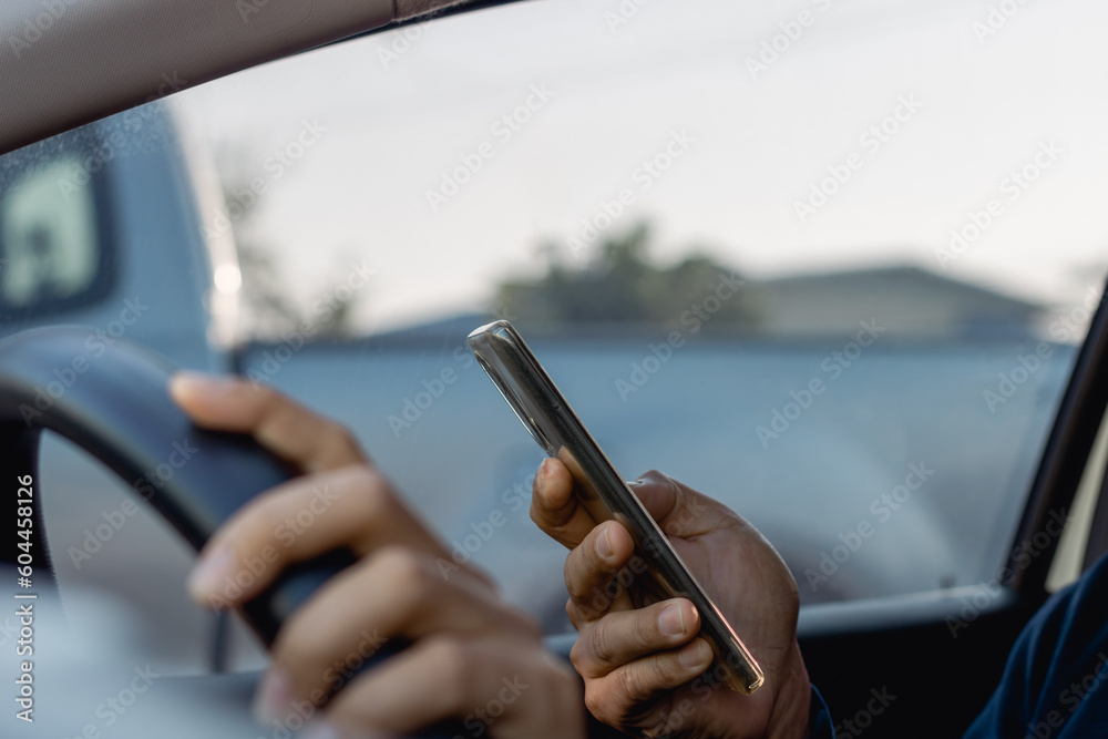 A man sitting in a car in the driver's seat looking into a smartphone, ignoring safety and texting on a mobile phone while driving. Man using the smartphone is essential in everyday life.