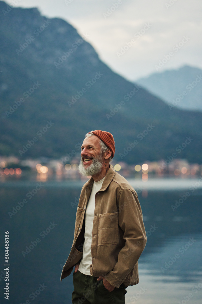 Happy older man standing in nature park enjoying natural park landscape view. Smiling mature active traveler exploring camping tourism nature lake and mountain travel feeling freedom. Vertical