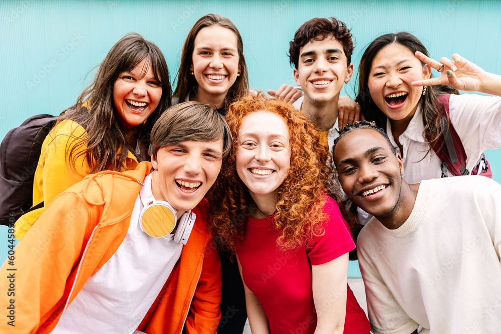 Diverse group of teenage student friends standing together over blue background. Portrait of young multiracial college people team having fun smiling at camera. Youth community and friendship concept