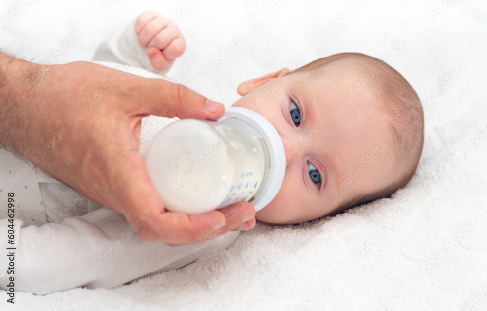 Baby eats formula from a bottle supported by his father Baby eats formula from a bottle supported by his father