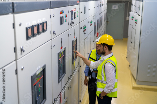 Professional electrical engineer in safety uniform working at factory server electric control panel room. Industrial technician worker maintenance checking power system at manufacturing plant room.