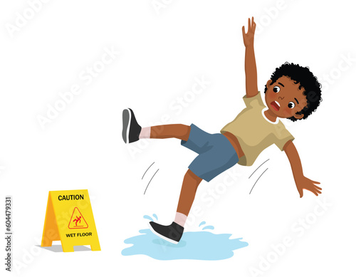 Cute little African boy having accident slipping on wet floor and falling down near yellow caution sign
