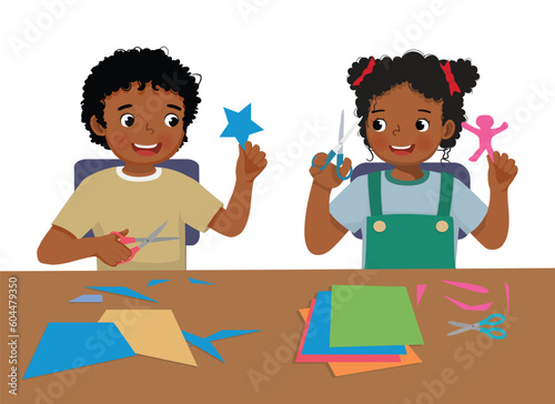 Cute little African kids boy and girl cutting colored paper with scissors making paper cut art craft
