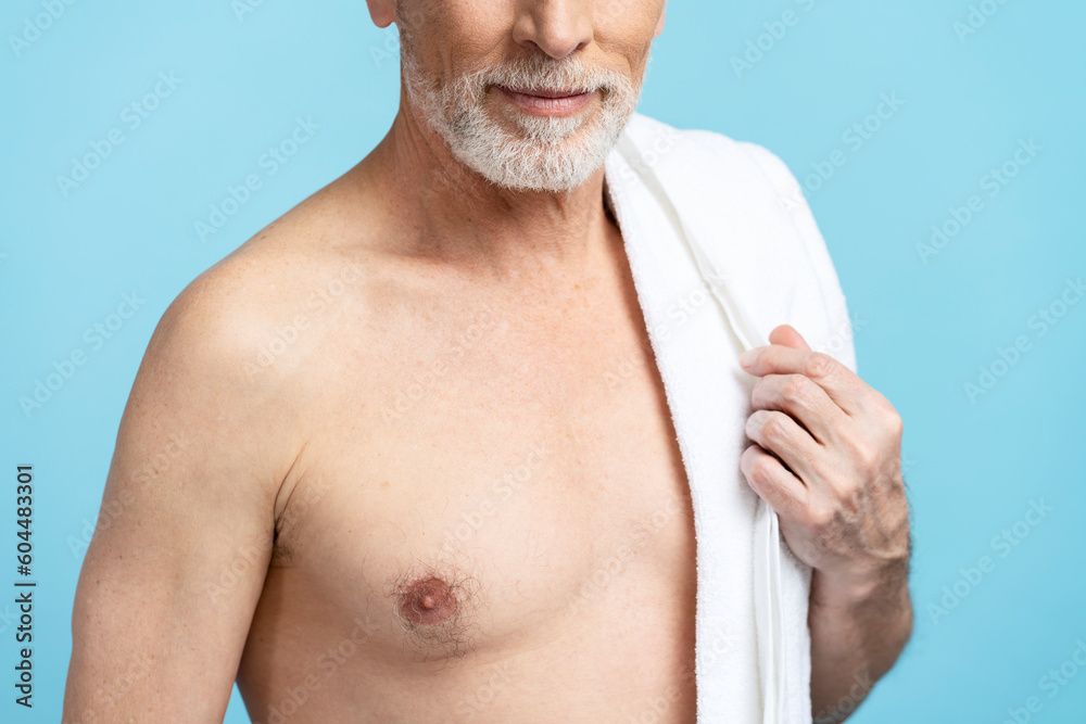 Portrait of senior pensioner with naked torso holding towel after shower isolated on blue background Portrait of senior pensioner with naked torso holding towel after shower isolated on blue background