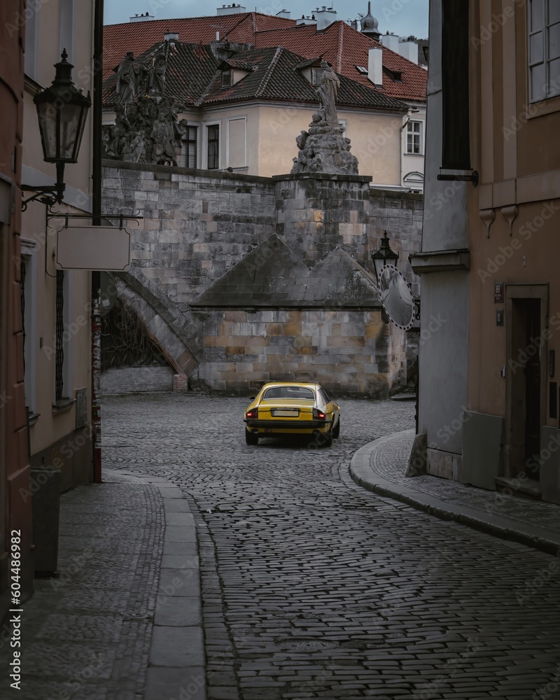 A view of a yellow retro car in the streets of Old Prague near Charles Bridge in the evening, in the center of Prague.