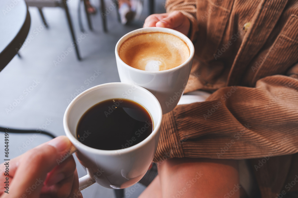 Closeup image of a couple people clinking white coffee mugs in cafe Closeup image of a couple people clinking white coffee mugs in cafe