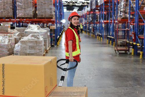 Warehouse worker woman with hardhats and reflective jackets pulling a pallet truck and taking or upload with large box package to shelf in retail warehouse logistics, distribution center © feeling lucky