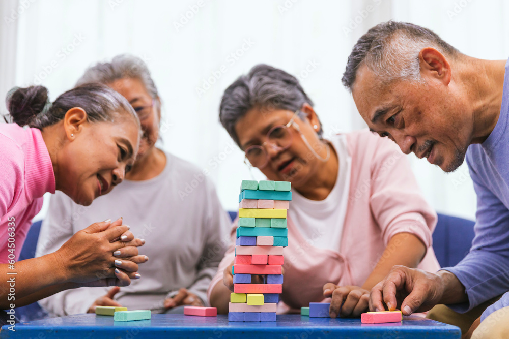 Senior people playing a wooden block tower, risk and strategy of project management. Concept of business risk with domino blocks. Older People playing jenga block removal game on table at home Senior people playing a wooden block tower, risk and strategy of project management. Concept of business risk with domino blocks. Older People playing jenga block removal game on table at home