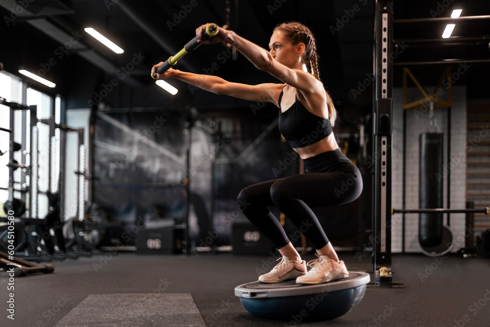 Sporty woman making squats on balance trainer.