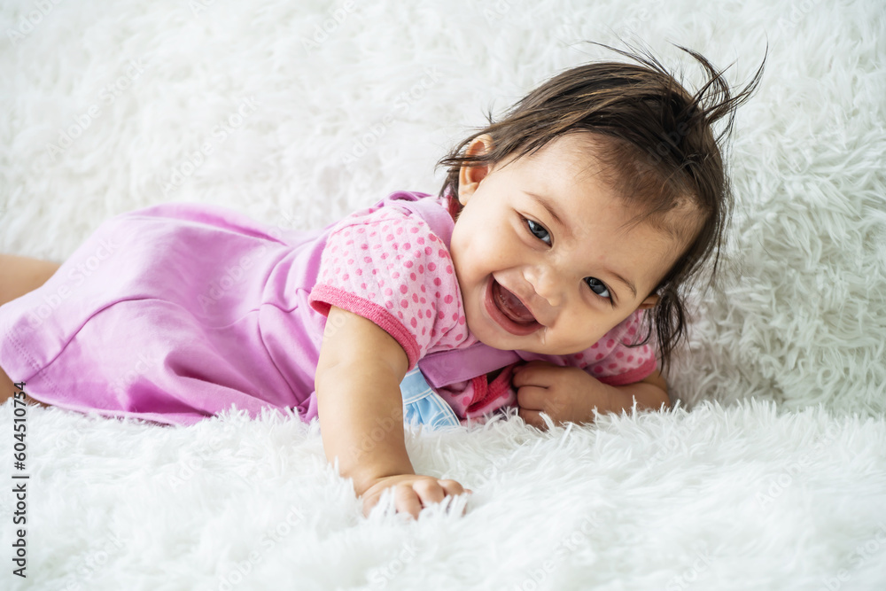 Childcare Concept. Portrait of cute little mixed race baby girl smiling and lying on white bed sheets at home. infant child crawling on bed in the bedroom. Selective focus