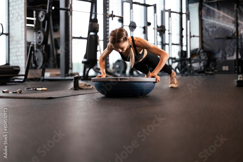 Portrait of a muscular woman on a plank position with bosu at gym.