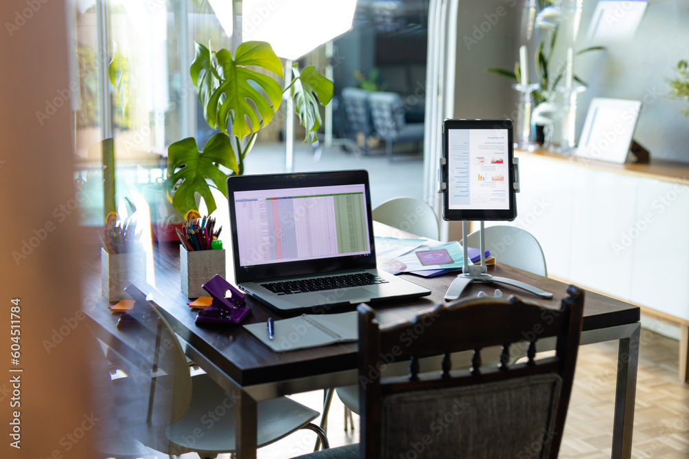 Notepad, laptop and tablet with spreadsheet and document on screen, on dining table in home office