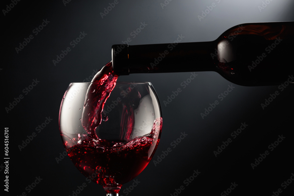 Pouring red wine into a wine glass. - obrazy, fototapety, plakaty 