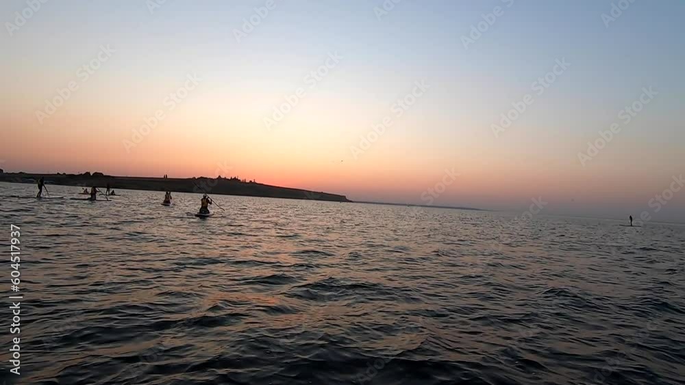 Man floating on SUP board at dawn sunset. Person floats on white SUP board and paddles rowing oar on sea surface with waves near shore on sunrise sundown. Active lifestyle recreation leisure sport POV Man floating on SUP board at dawn sunset. Person floats on white SUP board and paddles rowing oar on sea surface with waves near shore on sunrise sundown. Active lifestyle recreation leisure sport POV