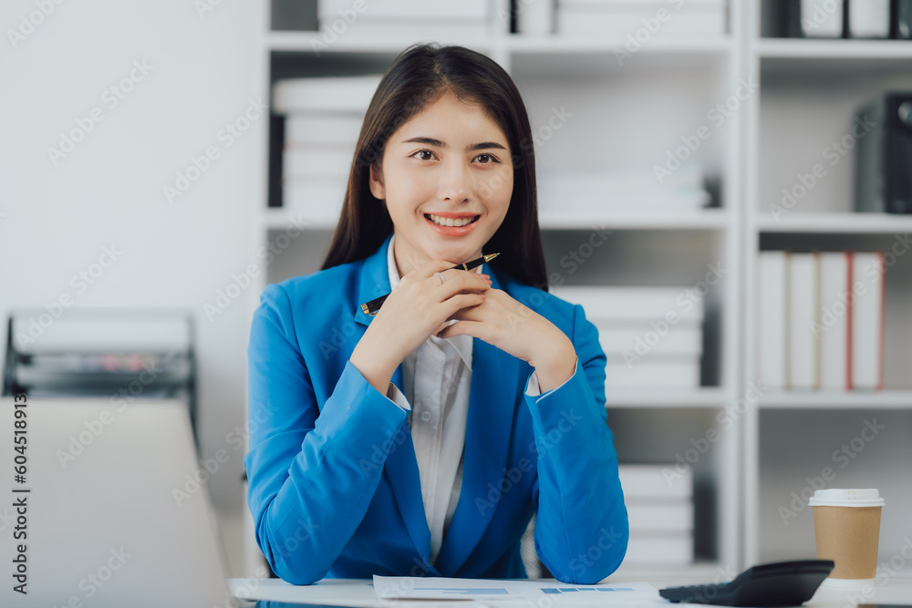 Asian Business woman using calculator and laptop for doing math finance on an office desk, tax, report, accounting, statistics, and analytical research concept