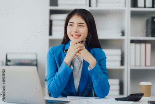 Asian Business woman using calculator and laptop for doing math finance on an office desk, tax, report, accounting, statistics, and analytical research concept